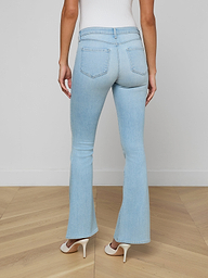 A woman stands facing away against a plain light background, showcasing the back of the Taney Low-Rise Flare Jean in light blue stretch denim, paired with white heels.