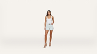 A woman in a white tank top, light blue shorts, and high-heeled sandals stands against a plain white background.