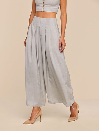 Wearing the Ysola Pant in light gray wool blend, paired with a matching sleeveless cropped top and beige high-heeled shoes, a woman stands against a plain beige background.