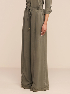 Une personne portant un pantalon Connie Drawstring en vert olive et une chemise à manches longues assortie se tient debout sur un fond beige uni.