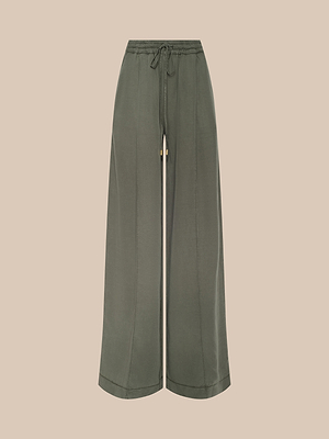 Le pantalon Connie à cordon de serrage présente des jambes larges, une taille haute et des accents dorés dans un sergé vert olive léger avec un cordon de serrage à la taille, sur un fond beige uni.