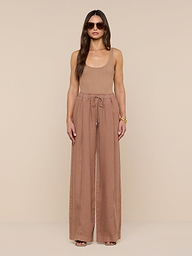 A woman stands facing forward against a plain white background, wearing sunglasses, a tan sleeveless top, and the Connie Linen Drawstring Trouser—loose, high-waisted linen pants with a drawstring waistband.