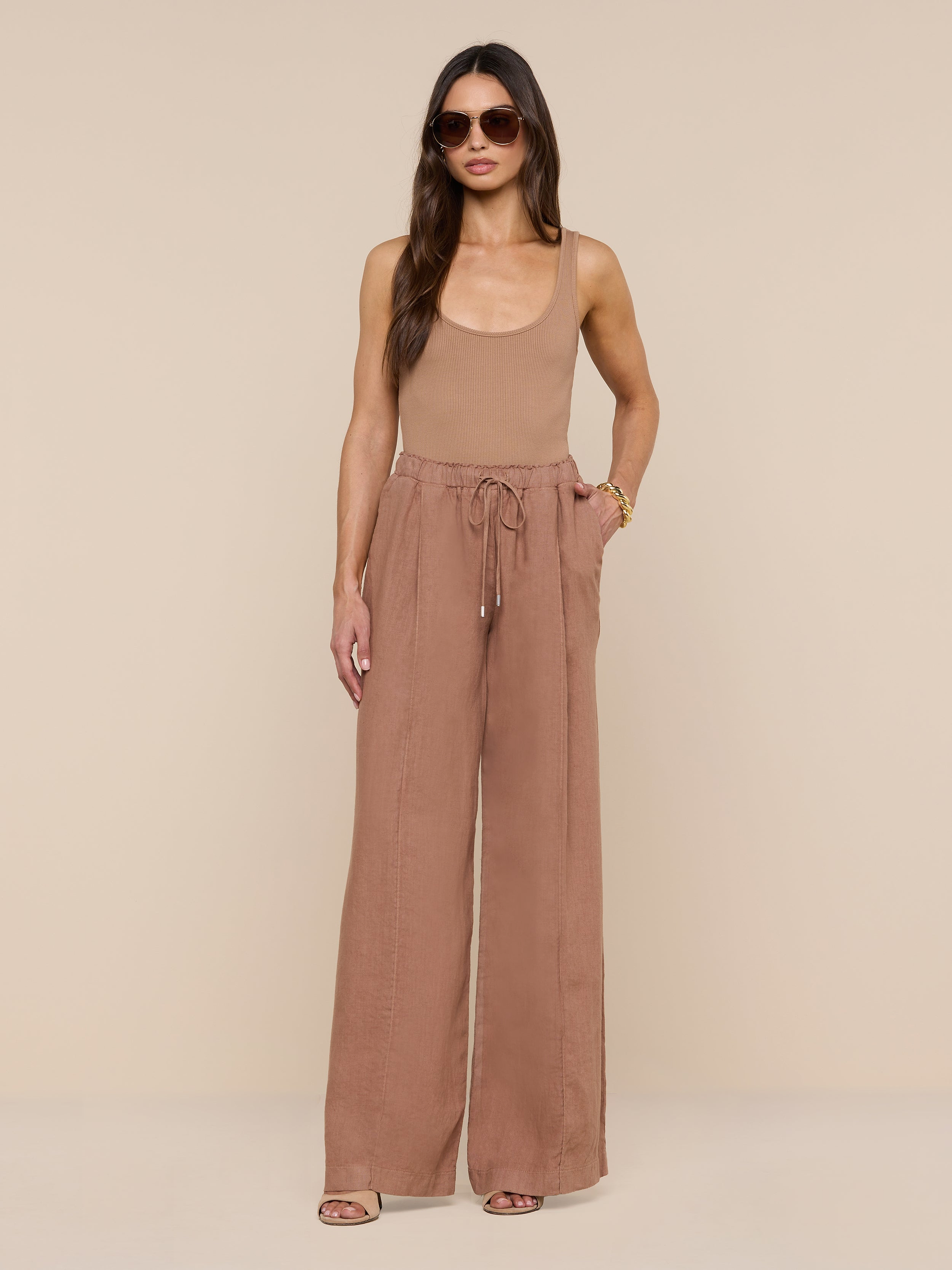 A woman wearing sunglasses, a sleeveless tan top, and the Connie Linen Drawstring Trouser—high-waisted, wide-leg vacation pants with a drawstring waistband—stands against a plain white background.