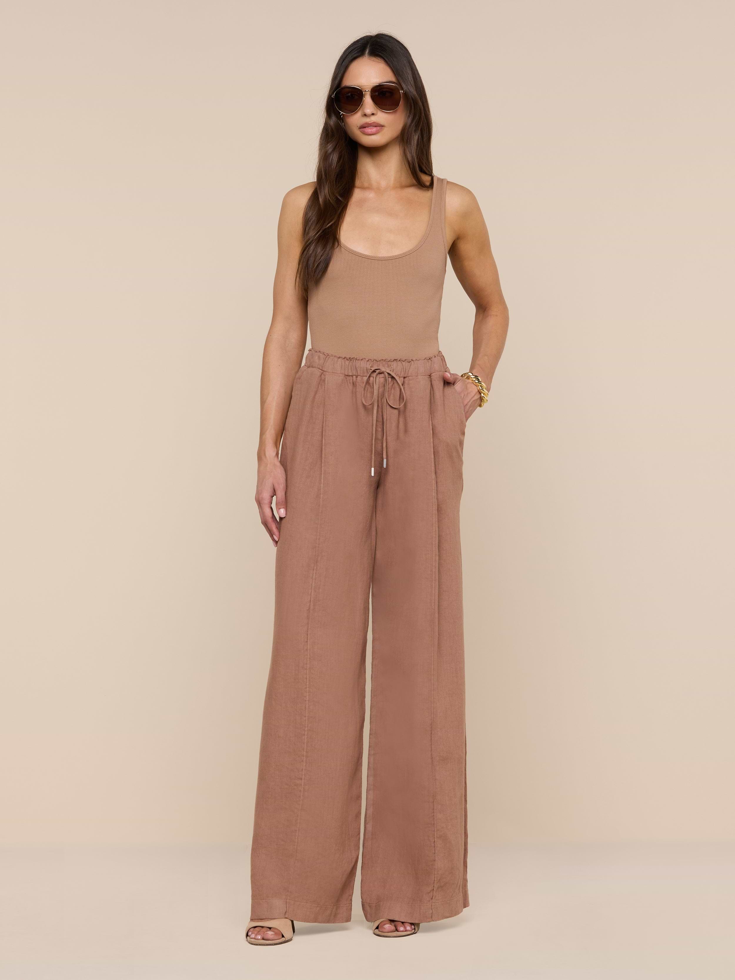 A woman wearing sunglasses, a sleeveless tan top, and the Connie Linen Drawstring Trouser—high-waisted, wide-leg vacation pants with a drawstring waistband—stands against a plain white background.
