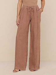 A person wearing the Connie Linen Drawstring Trouser—a wide-leg, high-waisted, light brown linen pant with a drawstring waistband—paired with a sleeveless top and heeled sandals, stands against a plain white background, with only the lower half of their body visible.