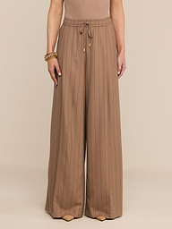 Mannequin portant le pantalon « Connie Drawstring » à fines rayures beiges, caractérisé par une taille haute, une coupe à jambes larges et un cordon de serrage à la taille, associé à un bracelet doré.