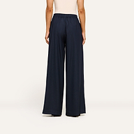 A person stands facing away, wearing a sleeveless beige top paired with the Connie Drawstring Trouser in navy blue—a refined and modern ensemble that captures a business casual style against a plain, light-colored background.