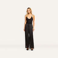 A woman stands facing forward, wearing the Mirel Satin Lace Pant with a V-neck sleeveless top and black shoes, against a plain light background.