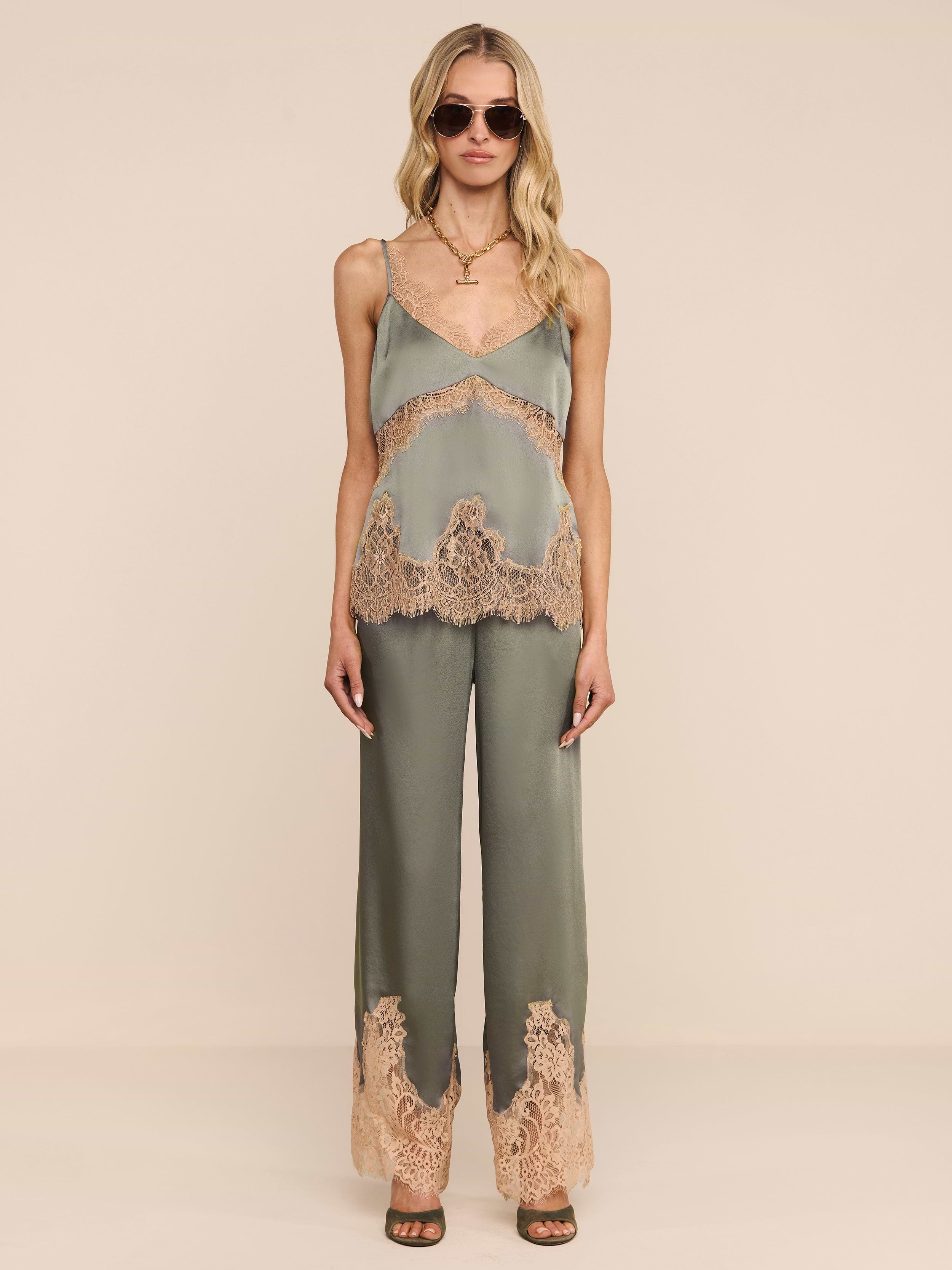 A woman stands against a plain white background wearing the Mirel Pant in olive green, featuring lace trim and a drawstring waist. She pairs it with a matching camisole, sunglasses, open-toe heels, and her long blonde hair.