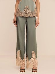 Wearing the Mirel Pant in olive green satin, featuring a drawstring waist and lace trim at the hem, paired with a coordinating top adorned with matching lace details, the individual is posed against a plain white backdrop.