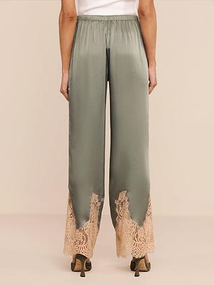 A person seen from the back wears Mirel Pant, featuring sage green satin, wide legs, beige lace-trimmed hems, and an elastic waistband. The pants are styled with heeled sandals.