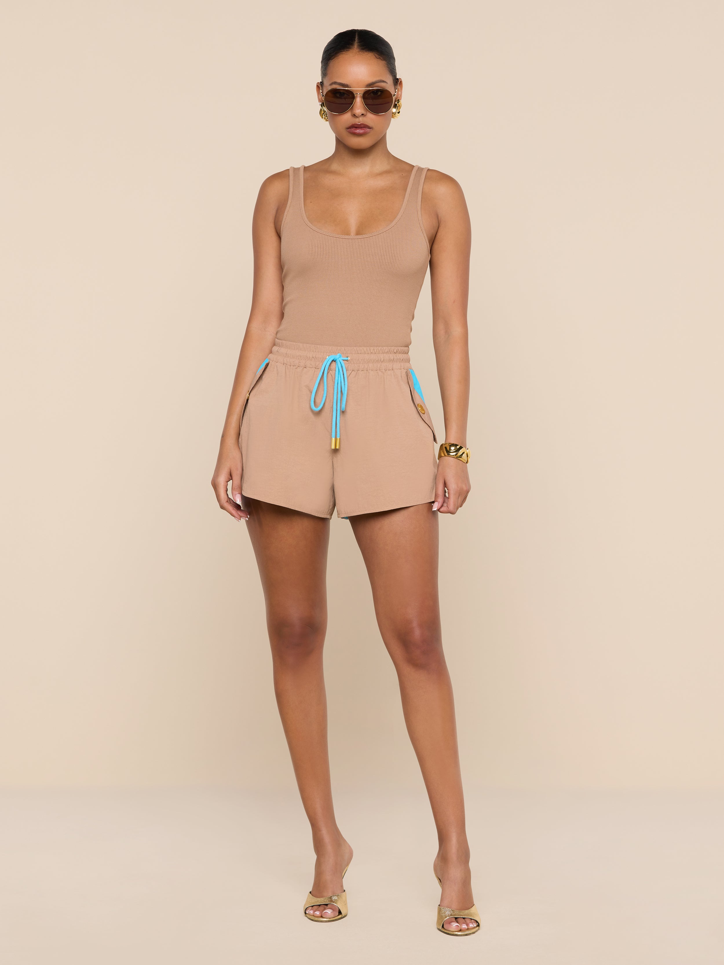 A woman in sunglasses wears a beige tank top and the Grayson Nylon Short, featuring a blue and yellow drawstring and crafted from water-repellent crepe nylon, standing against a plain white background.