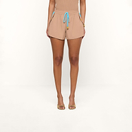 A person stands facing forward, wearing the Grayson Nylon Short in beige—crafted from water-repellent crepe nylon and featuring blue drawstrings—paired with a matching beige top. They wear open-toed sandals, set against a plain white background.