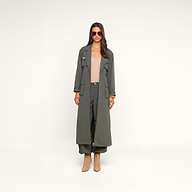 Woman wearing a long ash olive green trench coat with cargo pockets, Greer Nylon Jogger pants in olive, a tan top, heeled tan boots, sunglasses, and gold bracelets, standing against a beige background.