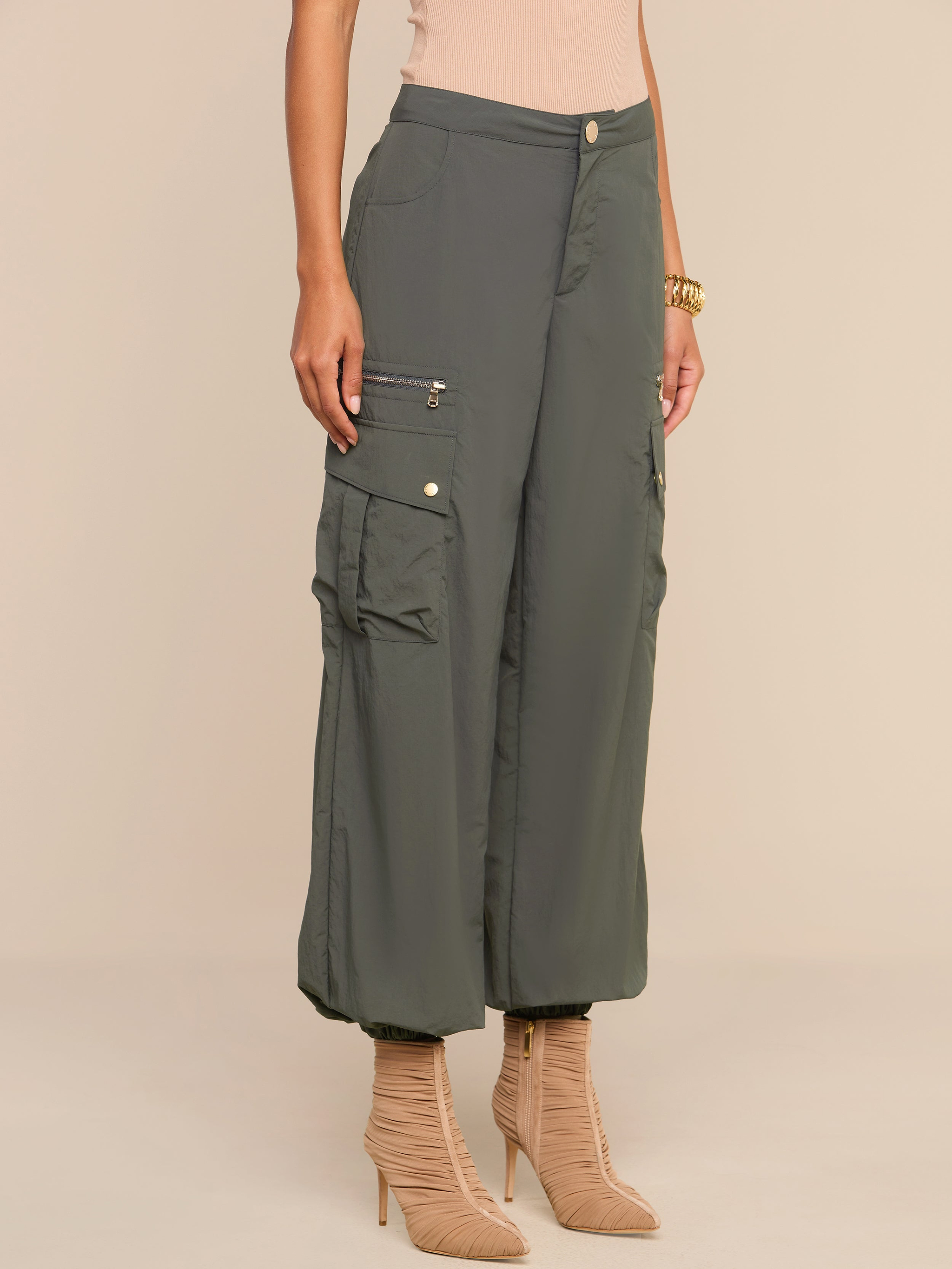 Wearing the Greer Nylon Jogger in ash olive green, featuring multiple cargo pockets, paired with beige high-heeled boots, a person stands against a neutral background.