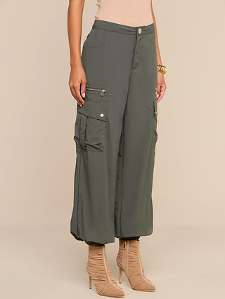 Wearing the Greer Nylon Jogger in ash olive green, featuring multiple cargo pockets, paired with beige high-heeled boots, a person stands against a neutral background.