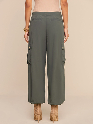 A person wearing the Greer Nylon Jogger in ash olive green and beige high-heeled sandals, standing with their back to the camera against a plain background.