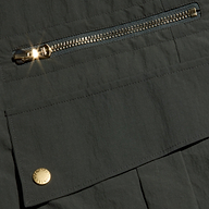 Close-up of the Greer Nylon Jogger in dark ash olive green, featuring a shiny metal zipper and snap button on a flap pocket—both catching the light. The design includes hints of cargo pockets that reflect its modern jogger style.