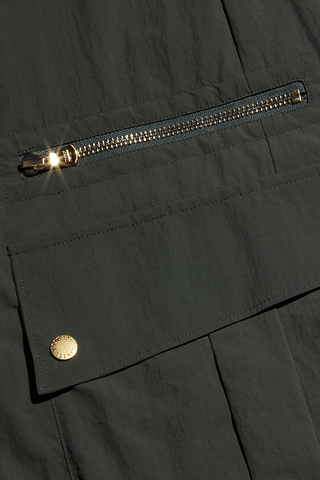 Close-up of the Greer Nylon Jogger in dark ash olive green, featuring a shiny metal zipper and snap button on a flap pocket—both catching the light. The design includes hints of cargo pockets that reflect its modern jogger style.