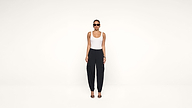 A woman wearing sunglasses, a white tank top, black cargo pants, and black heels stands facing forward against a plain white background.