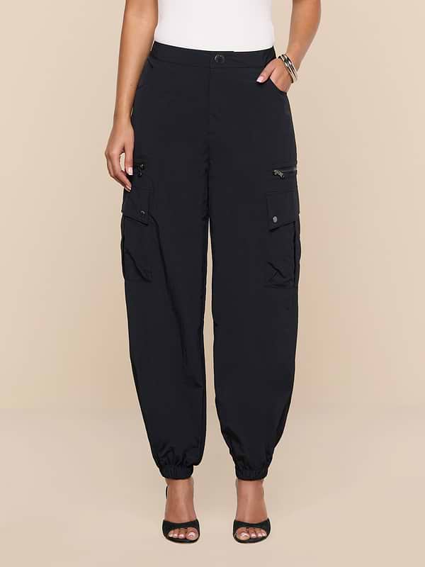 A person models the Greer Nylon Jogger—black cargo pants featuring cargo pockets—with black open-toe heels, standing against a plain white background. The top half of the body is cropped out of the frame.