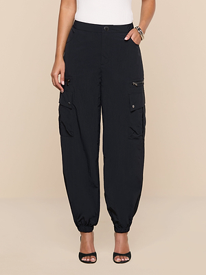 A person stands against a plain beige background wearing Greer Nylon Jogger pants in black with cargo pockets and ankle cuffs, styled with a white top, black open-toe heels, and bracelets.