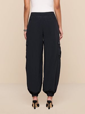 A person in Greer Nylon Jogger black cargo pants with elastic cuffs and cargo pockets, paired with high heels and a white sleeveless top, stands relaxed with arms by their sides, viewed from the back.