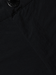 Close-up view of the black fabric on the Greer Nylon Jogger, showing detailed texture and stitching with a seam and a black button at the top left corner. The visible craftsmanship suggests modern design and potentially water-repellent material.