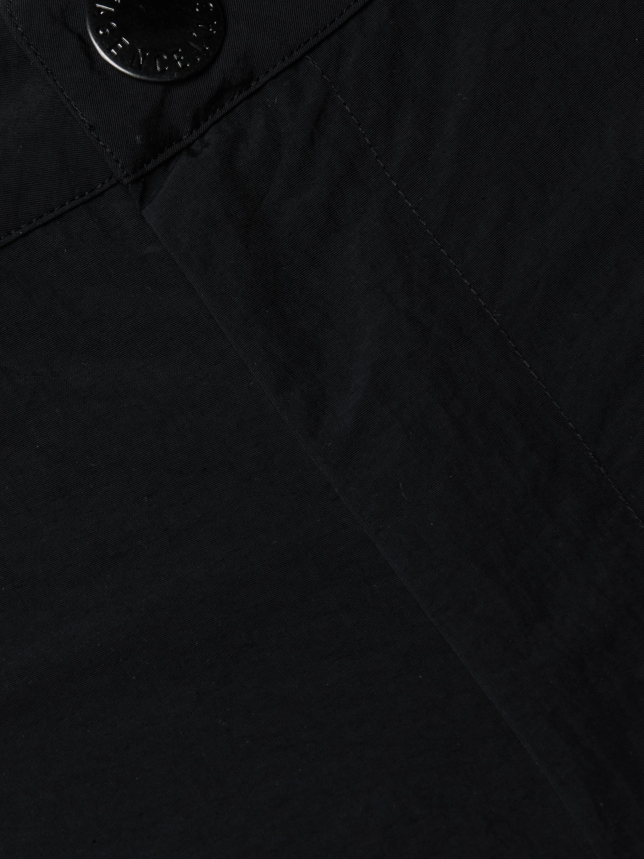 Close-up view of the black fabric on the Greer Nylon Jogger, showing detailed texture and stitching with a seam and a black button at the top left corner. The visible craftsmanship suggests modern design and potentially water-repellent material.