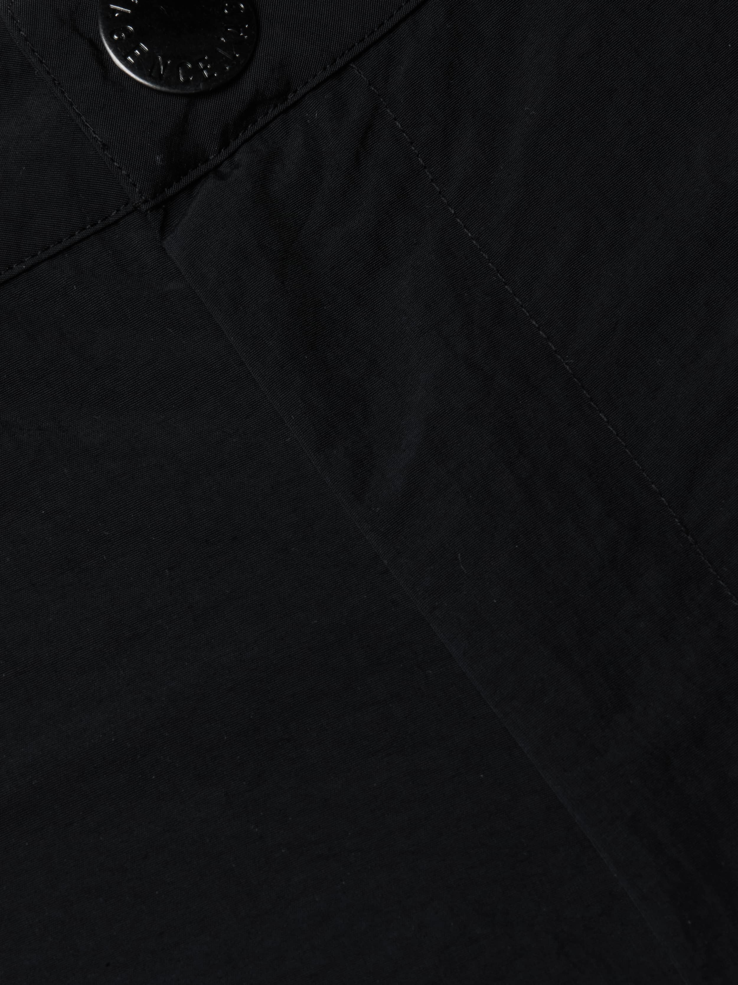 Close-up view of the black fabric on the Greer Nylon Jogger, showing detailed texture and stitching with a seam and a black button at the top left corner. The visible craftsmanship suggests modern design and potentially water-repellent material.
