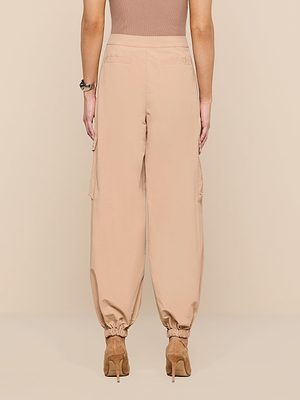 A person is shown from the back against a plain beige background wearing the Greer Nylon Jogger—modern, high-waisted beige cargo pants with elastic cuffs, cargo pockets—and tan heeled shoes.