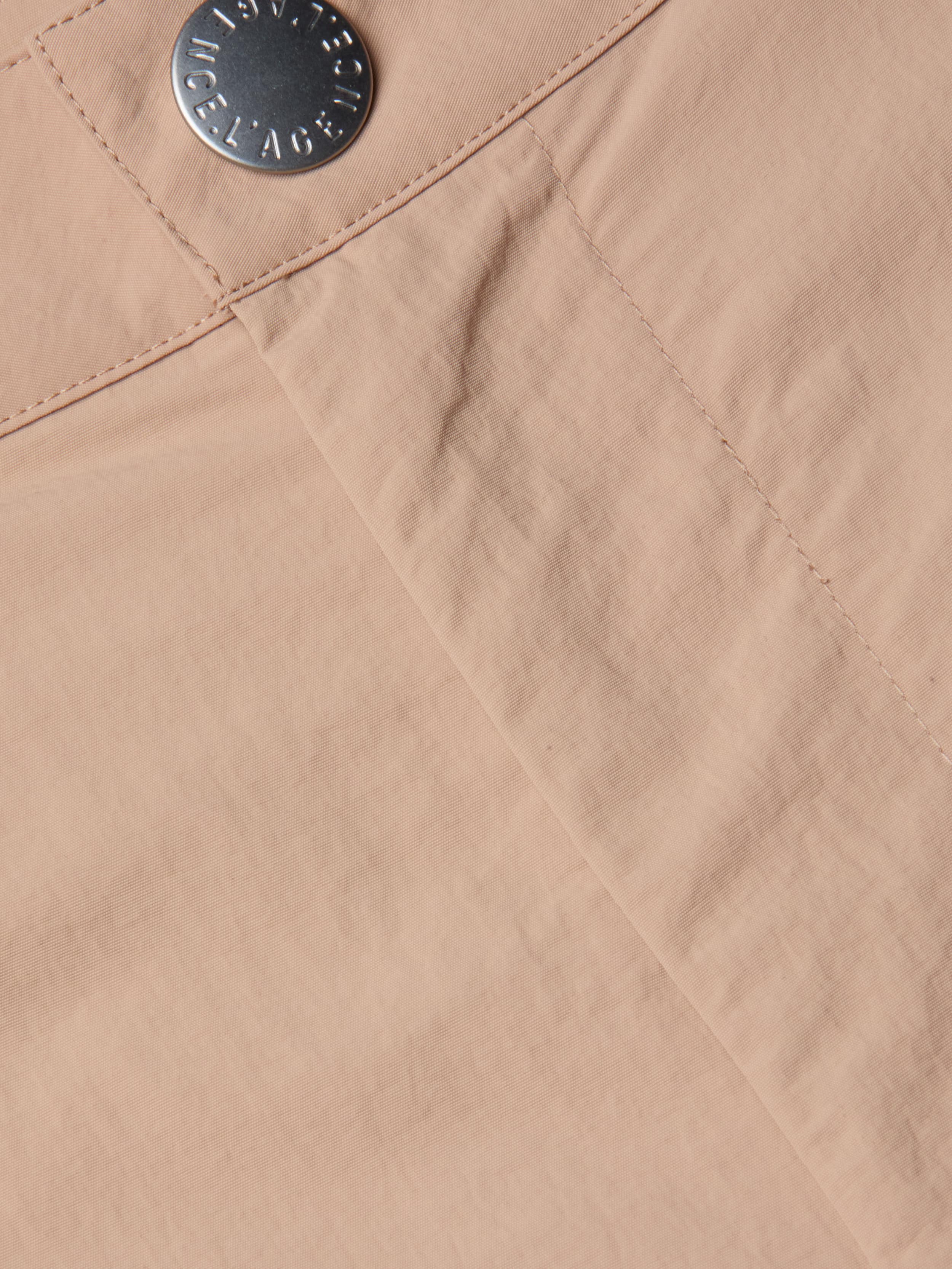 Close-up of the Greer Nylon Jogger in light beige fabric, showing visible stitching and a silver engraved button; features subtle cargo pockets for extra utility.