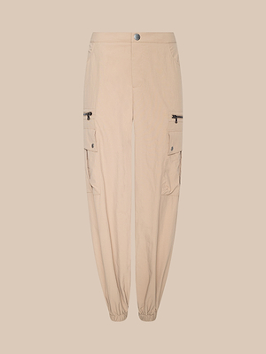 The Greer Nylon Jogger features elastic cuffs, cargo and side flap pockets with button closures, plus zippered pockets above the knees, shown on a beige background for a modern jogger style.
