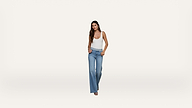 Woman with long hair wears a white tank top and high-waisted blue jeans, standing against a plain white background.