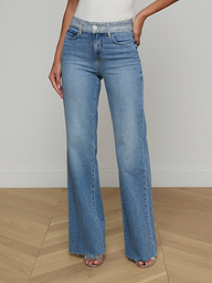 A woman models the Louane Wide-Leg Flare Jean in light blue, featuring a high-rise fit and frayed hems, paired with a white sleeveless top. She stands against a plain light background with her hands at her sides and her face out of view.