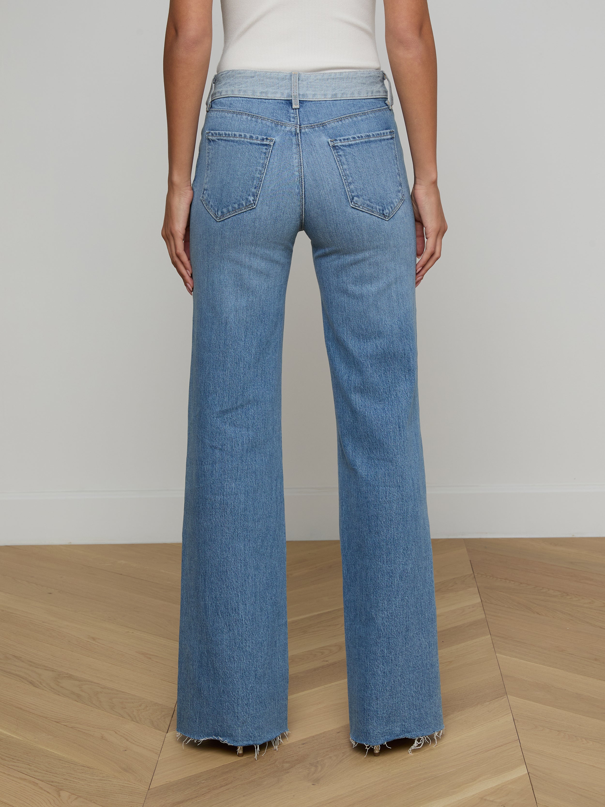 A person shown from the back is wearing Louane Wide-Leg Flare Jeans in a high-rise, light blue wash with frayed hems, paired with a white top.