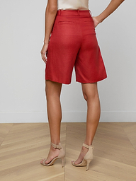 A woman stands with her back to the camera, wearing the Doretta Bermuda Short in a red linen blend, paired with a light-colored top and beige high-heeled sandals against a plain white background—perfect for summer-in-the-office style.