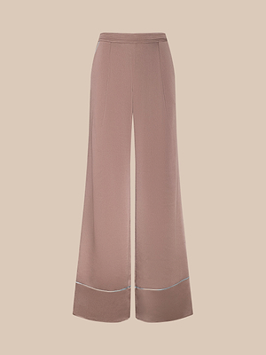The Tavia Satin Trouser features a wide-leg, high-waisted mauve design with subtle front seams and light blue contrast piping near the hem, shown on a neutral beige background.