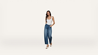 A woman wearing a white tank top, blue high-waisted wide-leg jeans with embellishments, and white heels stands against a plain white background.