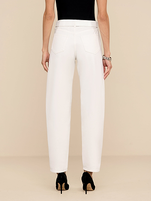 Una persona che indossa jeans a vita alta Bex Embellished Rodeo Jeans in bianco con scarpe nere con tacco, visti da dietro su uno sfondo beige, abbinati a un top nero senza maniche e a un braccialetto dargento.