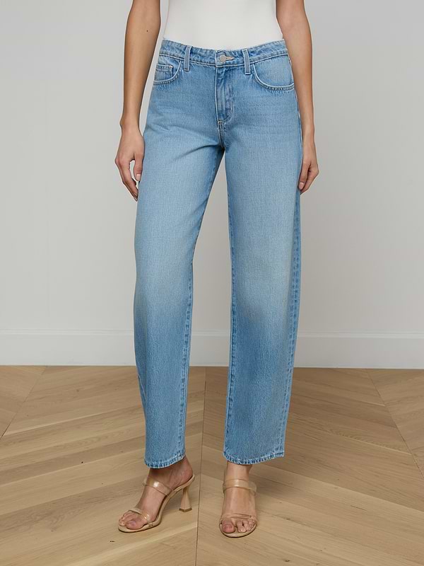 A person wearing the Bex Rodeo Jean in light blue all-cotton denim, paired with a white top and beige heeled sandals, standing against a plain light background.