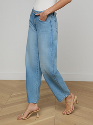 Wearing the Bex Rodeo Jean in light blue, a white top, and beige heeled sandals, a person stands against a plain light background.