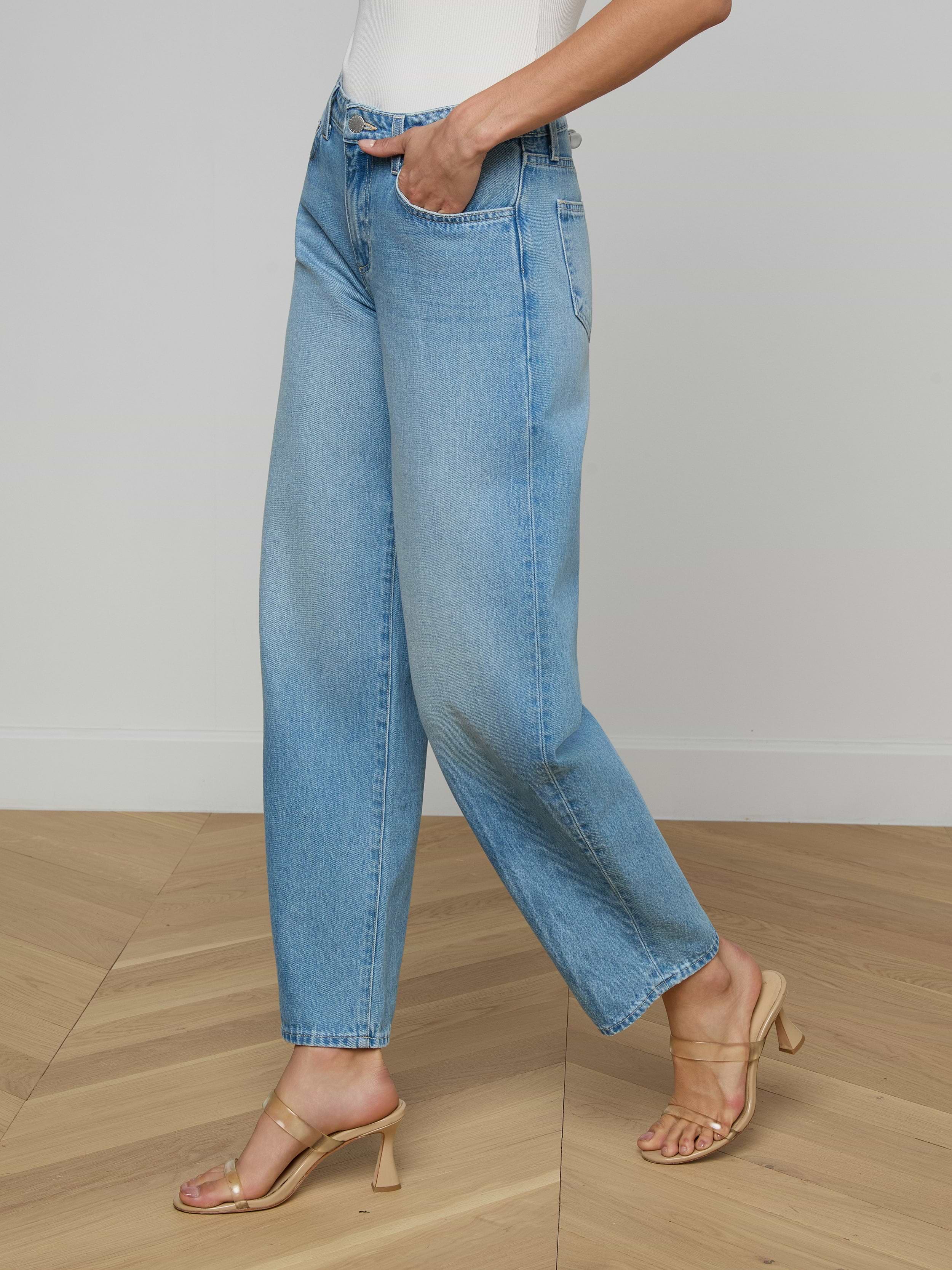 Wearing the Bex Rodeo Jean in light blue, a white top, and beige heeled sandals, a person stands against a plain light background.