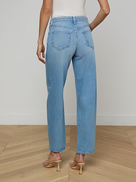 A person is shown from the back against a plain, light background wearing the Bex Rodeo Jean—a pair of light blue, high-waisted barrel leg jeans crafted from all-cotton denim—paired with heeled sandals.