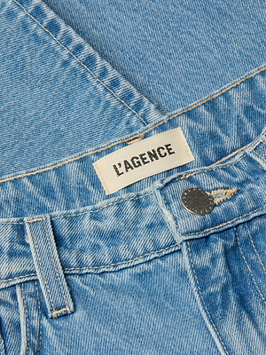 Close-up of the Bex Rodeo Jean in light blue vintage denim, featuring a high rise waistband, belt loop, metallic button, and a white fabric label with L’AGENCE in black uppercase letters.
