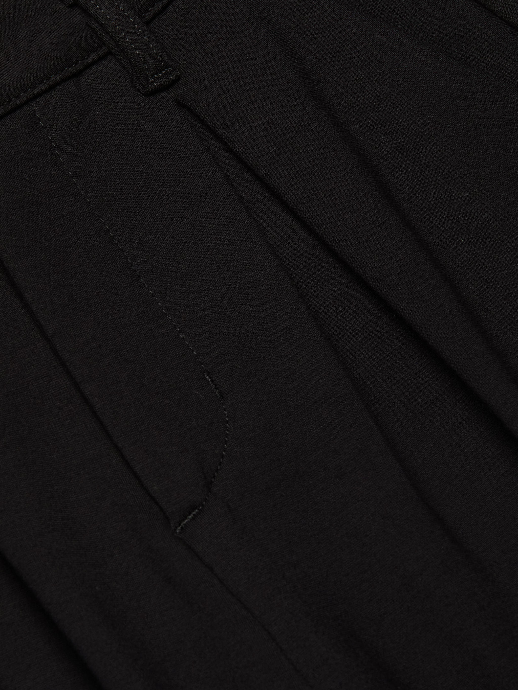Close-up of the Akasha Bermuda Short in black stretch ponte fabric, featuring a seam, waistband with a belt loop, and pleated detailing.