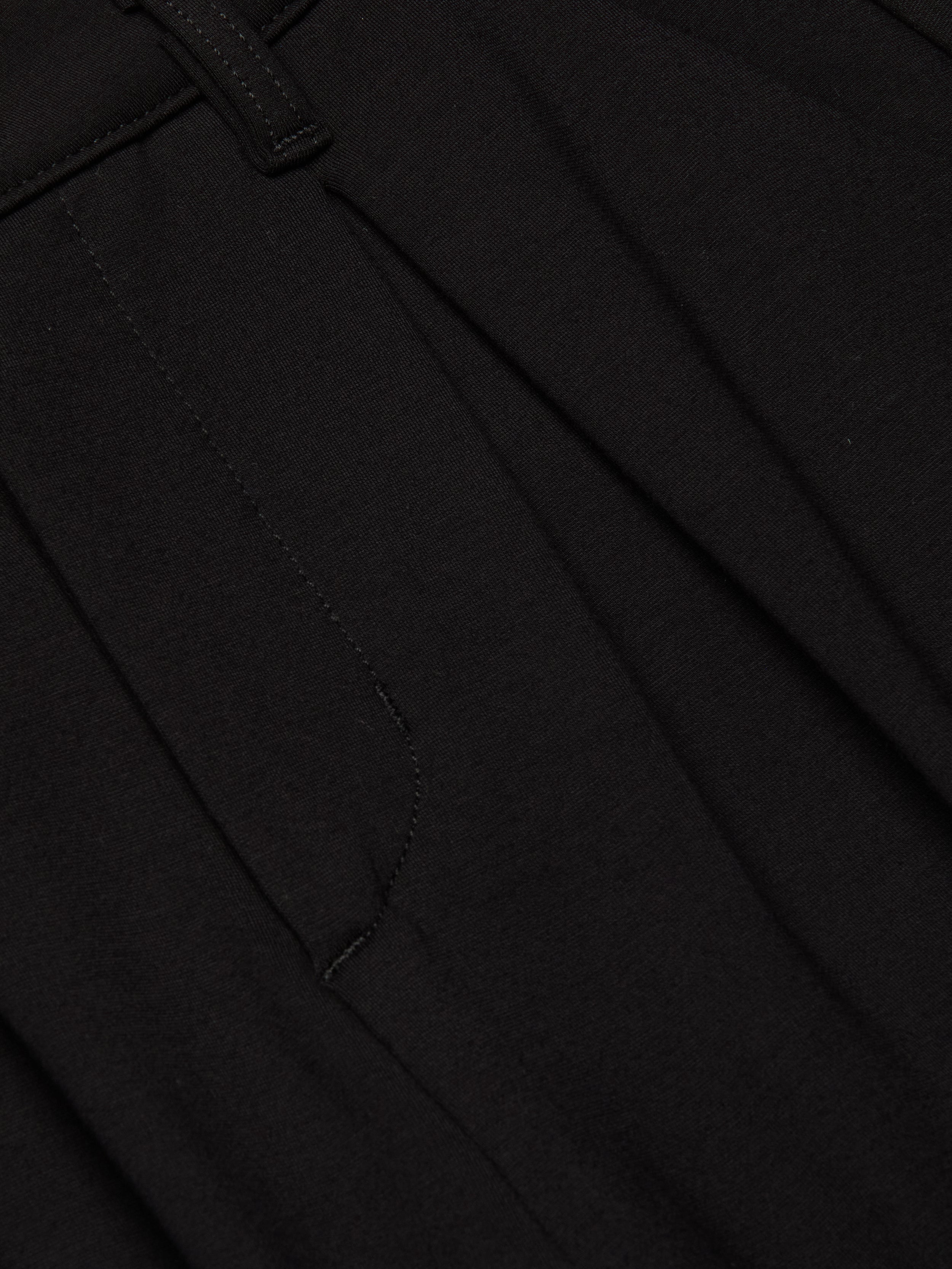 Close-up of the Akasha Bermuda Short in black stretch ponte fabric, featuring a seam, waistband with a belt loop, and pleated detailing.