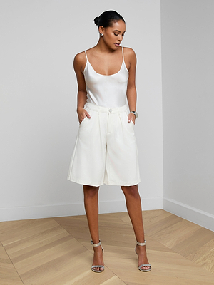 Woman wearing a white sleeveless top and shorts on a plain background