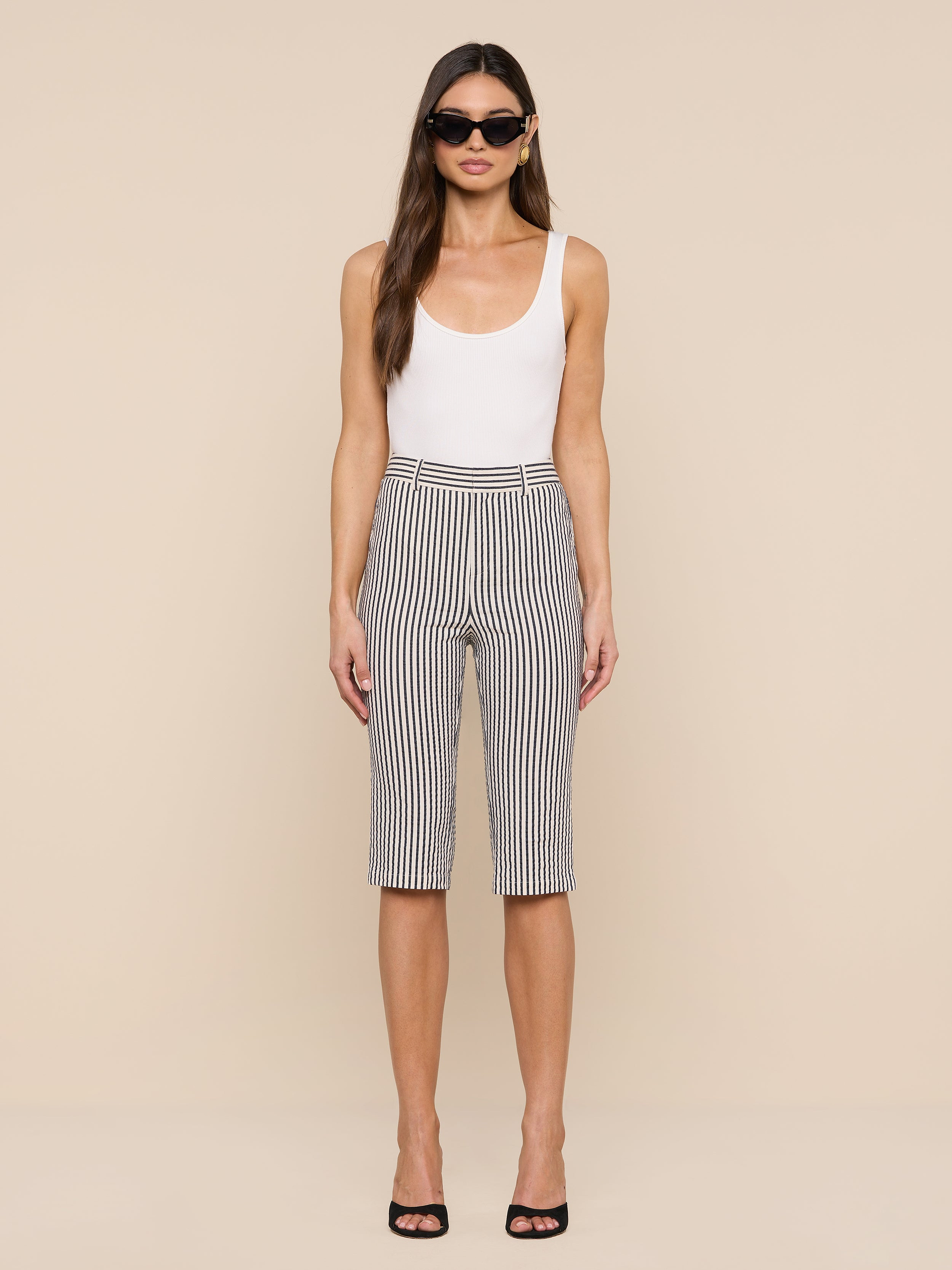 A woman stands facing forward against a plain white background, wearing sunglasses, a white tank top, and the Leni Pedal Pusher in black and white stripes.