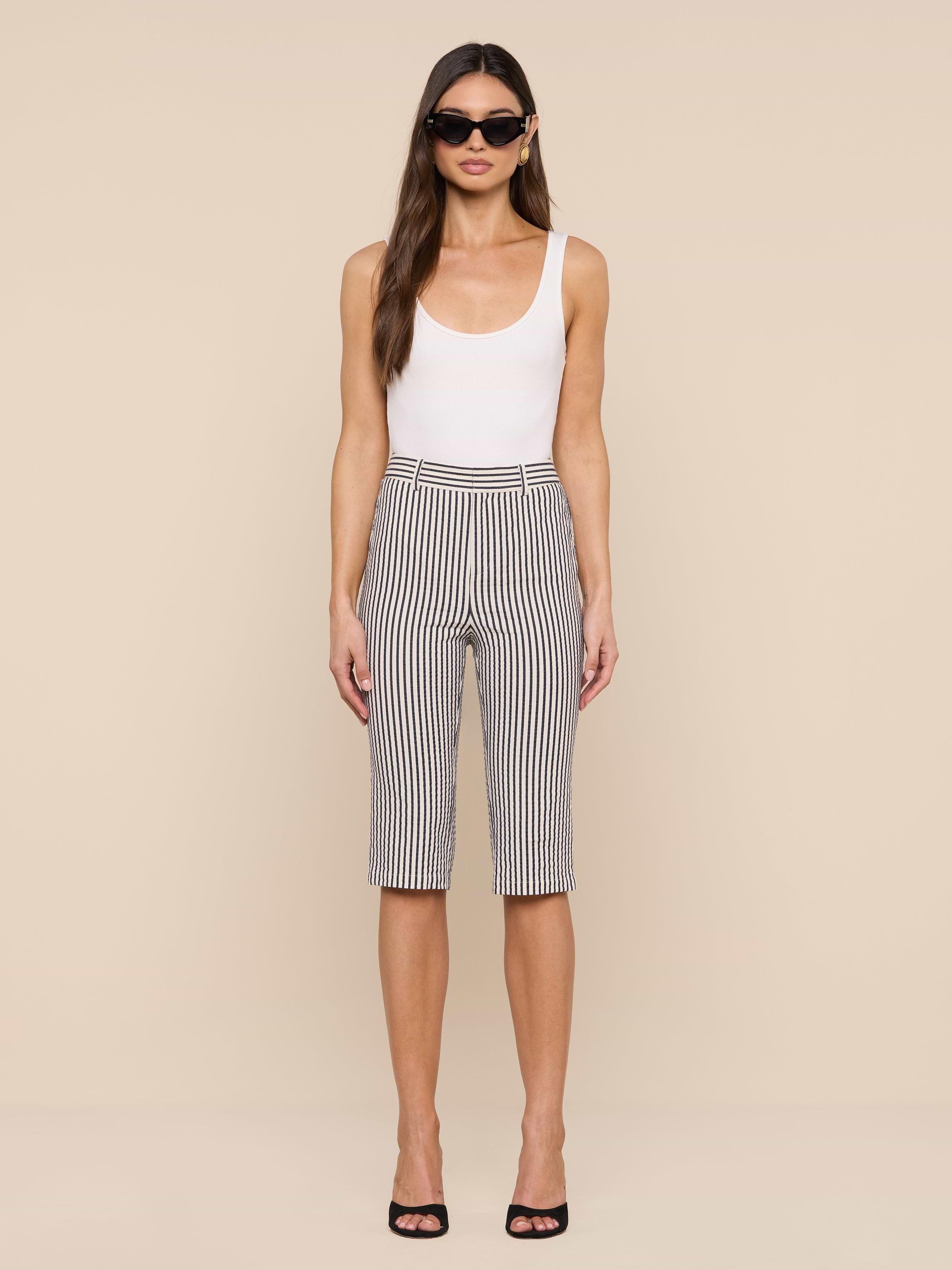 A woman stands facing forward against a plain white background, wearing sunglasses, a white tank top, and the Leni Pedal Pusher in black and white stripes.